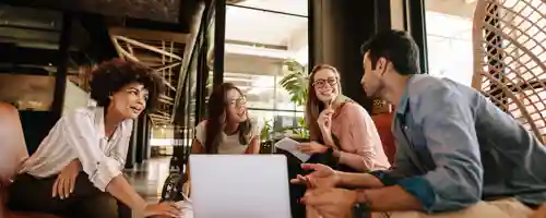 Four people sitting at a table with computers and papers talking
